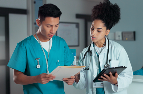 A doctor stands with a nurse looking at paperwork in a file.